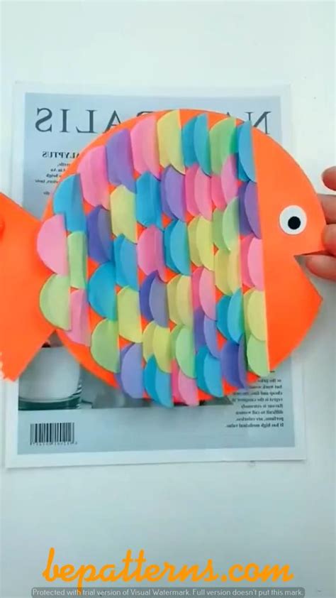 a person holding up a fish made out of construction paper and colored glue on top of a magazine