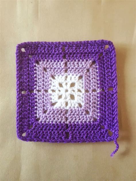 a crocheted square is sitting on a table with a white and purple border