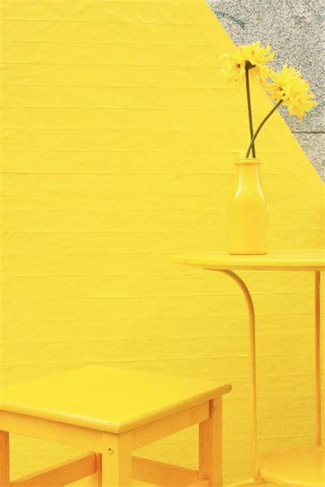 a yellow table and two small tables with flowers in a vase on them against a wall
