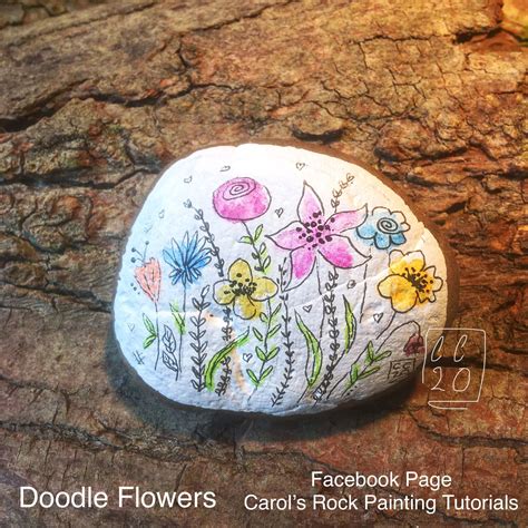 a rock with flowers painted on it sitting on a piece of wood that is ...