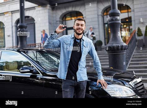 Handsome man standing in front of black car and presenting it Stock Photo - Alamy