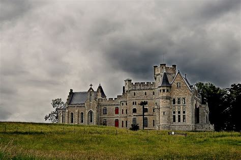 an old castle sitting on top of a lush green hillside under a cloudy sky with dark clouds