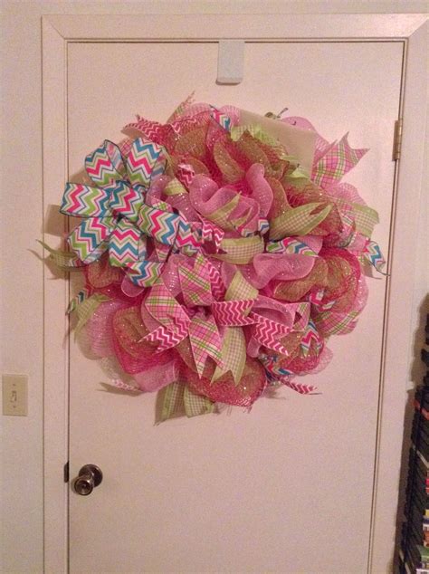 a pink and green mesh wreath hanging on the front door to a white door way