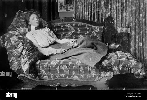 A young Victorian woman takes a break from reading her poetry while lounging on a fainting couch ...