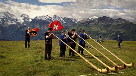 People in traditional Swiss costume blow Alphorns with a Swiss flag and a backdrop of snow : r/pics