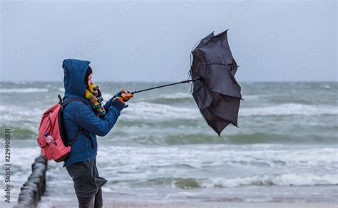 strong wind destroys a woman's umbrella during a beach walk Stock Photo | Adobe Stock