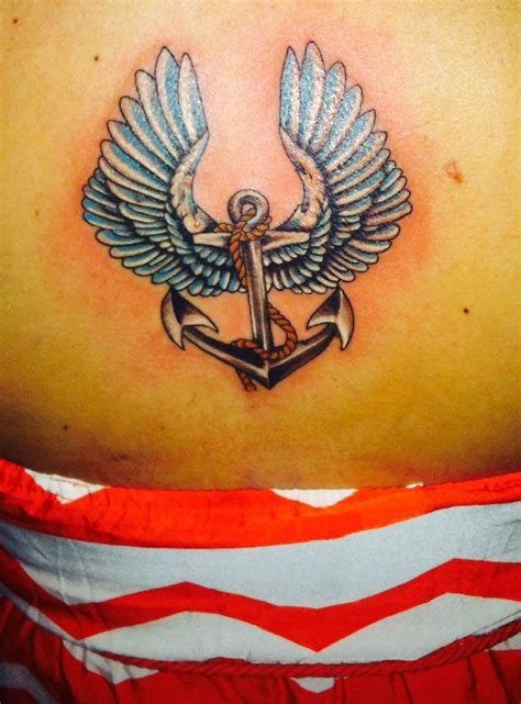 the back of a woman's shoulder with an anchor and wings tattoo