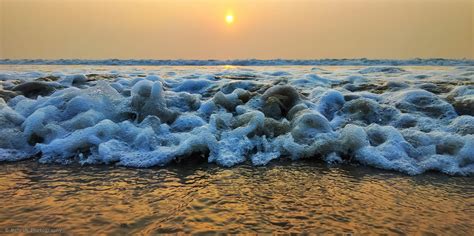 the sun is setting over an ocean with foamy waves in the foreground and ...