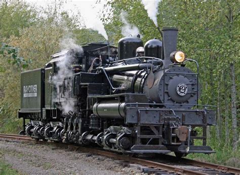 an old fashioned steam engine traveling down the tracks in front of some trees and bushes