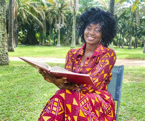 Jeune femme africaine souriante tenant un livre en plein air - Photo ...