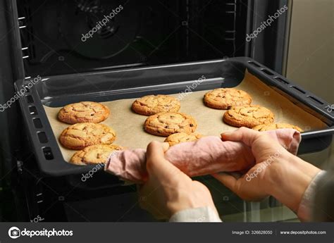 Woman taking baking tray with cookies out of oven Stock Photo by ...
