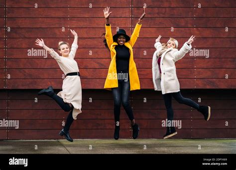 Three happy girlfriends jumping in front of a wooden wall Stock Photo ...