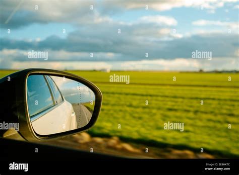 Through glass of side mirror of modern white car driving on asphalt ...