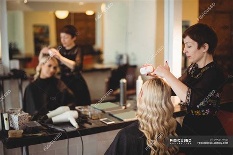 Female hairdresser styling clients hair in saloon — young adult ...