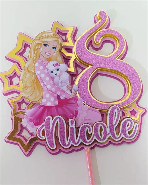 A Pink And Gold Birthday Cake Topper With A Barbie Doll Holding A Teddy