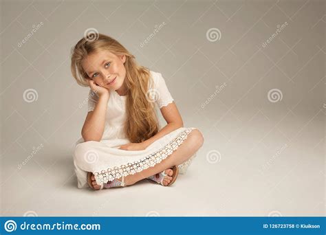 Petite Fille De Sourire Sasseyant Sur Le Fond De Studio Photo Stock