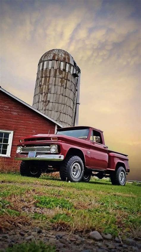 An Old Red Truck Parked In Front Of A Barn With A Silo Behind It