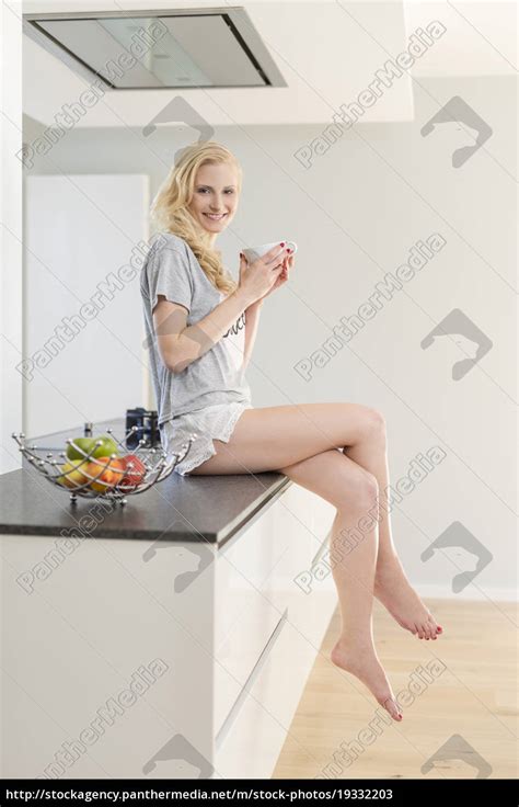 Smiling Blond Woman Sitting On Kitchen Counter With Lizenzfreies Bild 19332203