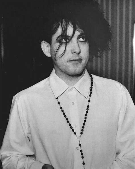 A Man With Long Hair Wearing A White Shirt And Black Beaded Necklace