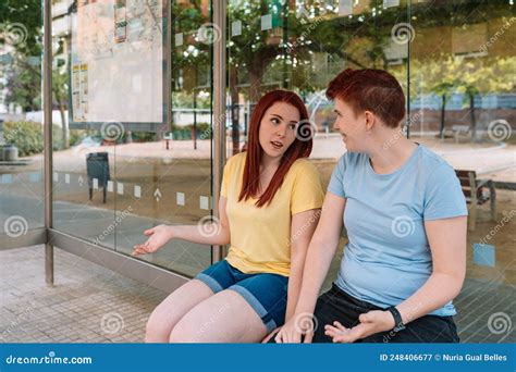 Two Happy Young Friends Sitting At The Bus Stop Talking And Gossiping