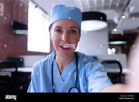 Caucasian Female Doctor Wearing Scrubs Sitting At Desk Talking During