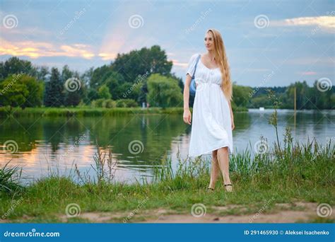 Young Woman In Long White Dress Standing On The River Bank During