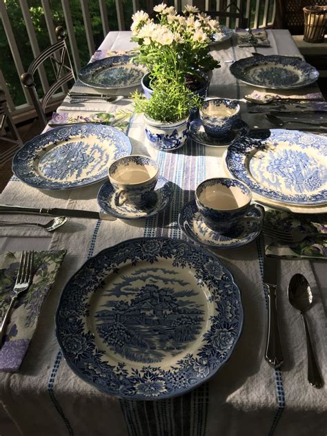 The Table Is Set With Blue And White China Plates Silverware And Flowers