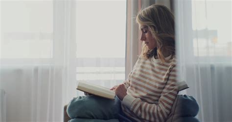 Attractive Woman Reading Book While Sitting On A Sofa At Home Feels