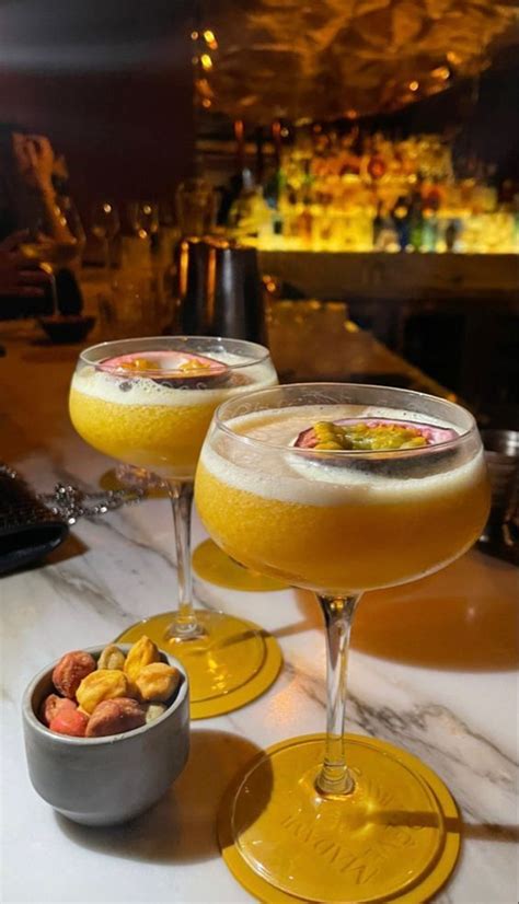 Two Glasses Filled With Drinks Sitting On Top Of A Table Next To Bowls