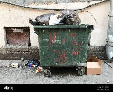 Green dirty trash dumpster, front view, next to the wall of the old building. Opened city trash ...