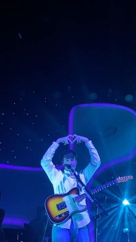 A Man Standing On Stage With His Hands Up In The Air While Holding A Guitar