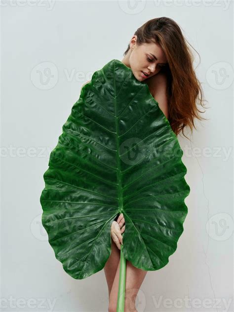 Red Haired Woman Covers Naked Body With Palm Leaf Light Background