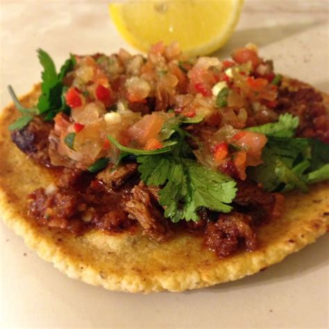 A Tortilla Topped With Meat And Cilantro Next To A Lemon Wedge