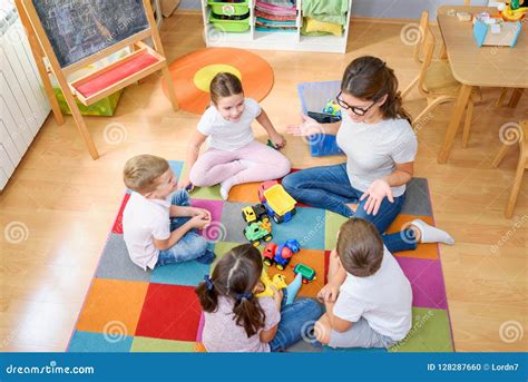 Preschool Teacher Talking To Group Of Children Sitting On A Floor At