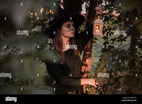 Young Woman In Dark Dress And Witchs Hat Holds Lantern With Candles In