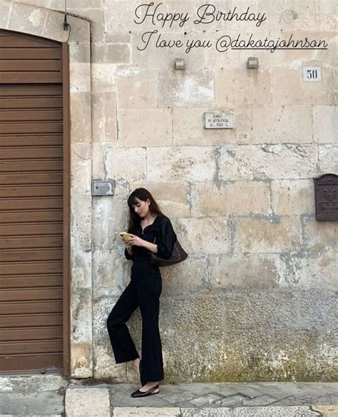 A Woman Leaning Against A Wall With Her Cell Phone