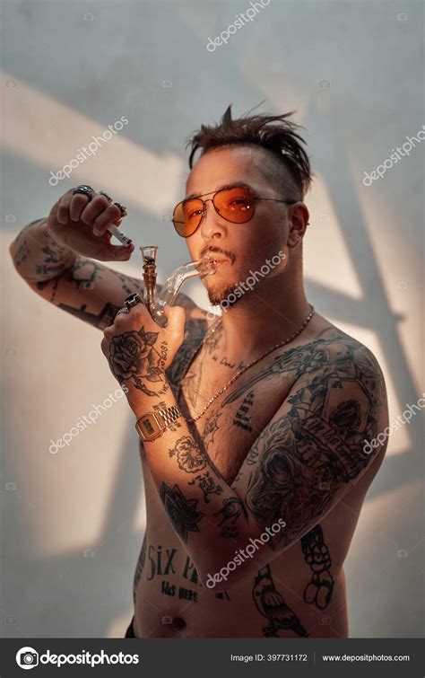 Shirtless Man With Tattooed Body And Freaky Haircut Lighting Cannabis