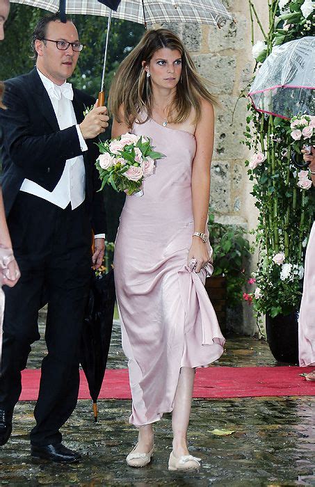 A Man In A Tuxedo And Woman In Pink Dresses Walking Under An Umbrella