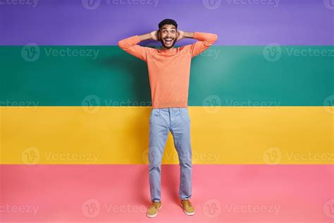 Excited African Man Holding Hands Behind Head While Standing Against Colorful Background