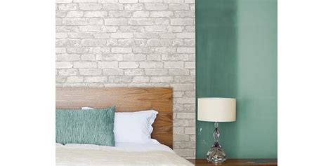 A Bed With White Sheets And Pillows Next To A Green Brick Wall In A Bedroom