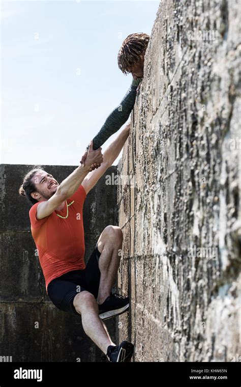 Young male free climber at top of sea wall helping friend climb up ...