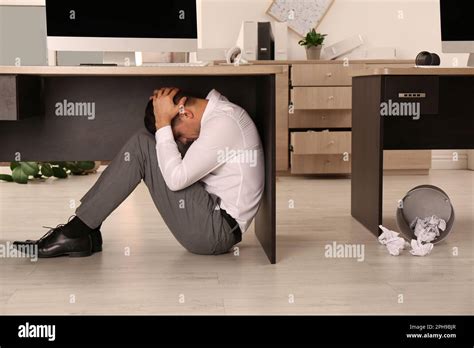 Scared Man Hiding Under Office Desk During Earthquake Stock Photo Alamy