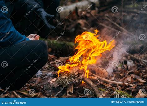 Man Warms His Hands On Fire Burning Wood At Evening In The Forest