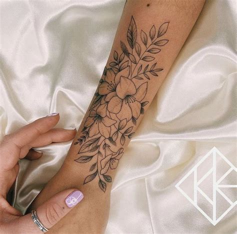 a woman's arm with flowers and leaves on it, while she is laying down