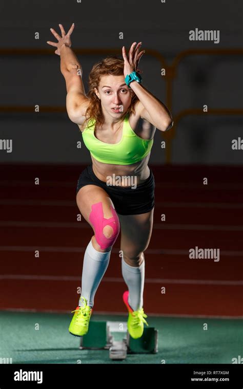 Female Athlete Starting Sprint Race Running From Blocks Against Dark