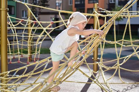 Una niña feliz jugando en una red de cuerdas en el patio de recreo