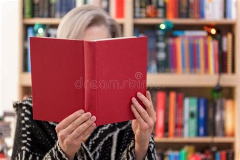 Woman Holding Book In Front Of Face On Blurred Bookshelf Background