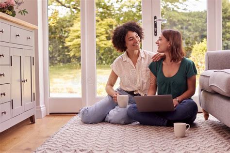 Same Sex Female Couple Or Friends At Home Sitting In Lounge Using Laptop And Drinking Coffee