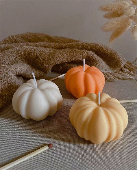 Three Pumpkin Candles Sitting On Top Of A Table Next To A Brown Blanket