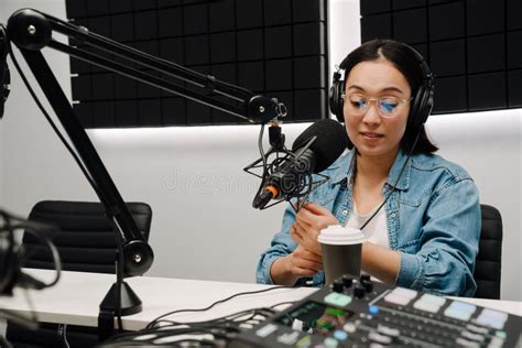 Young Female Radio Host Using Microphone And Headphones In Studio Stock